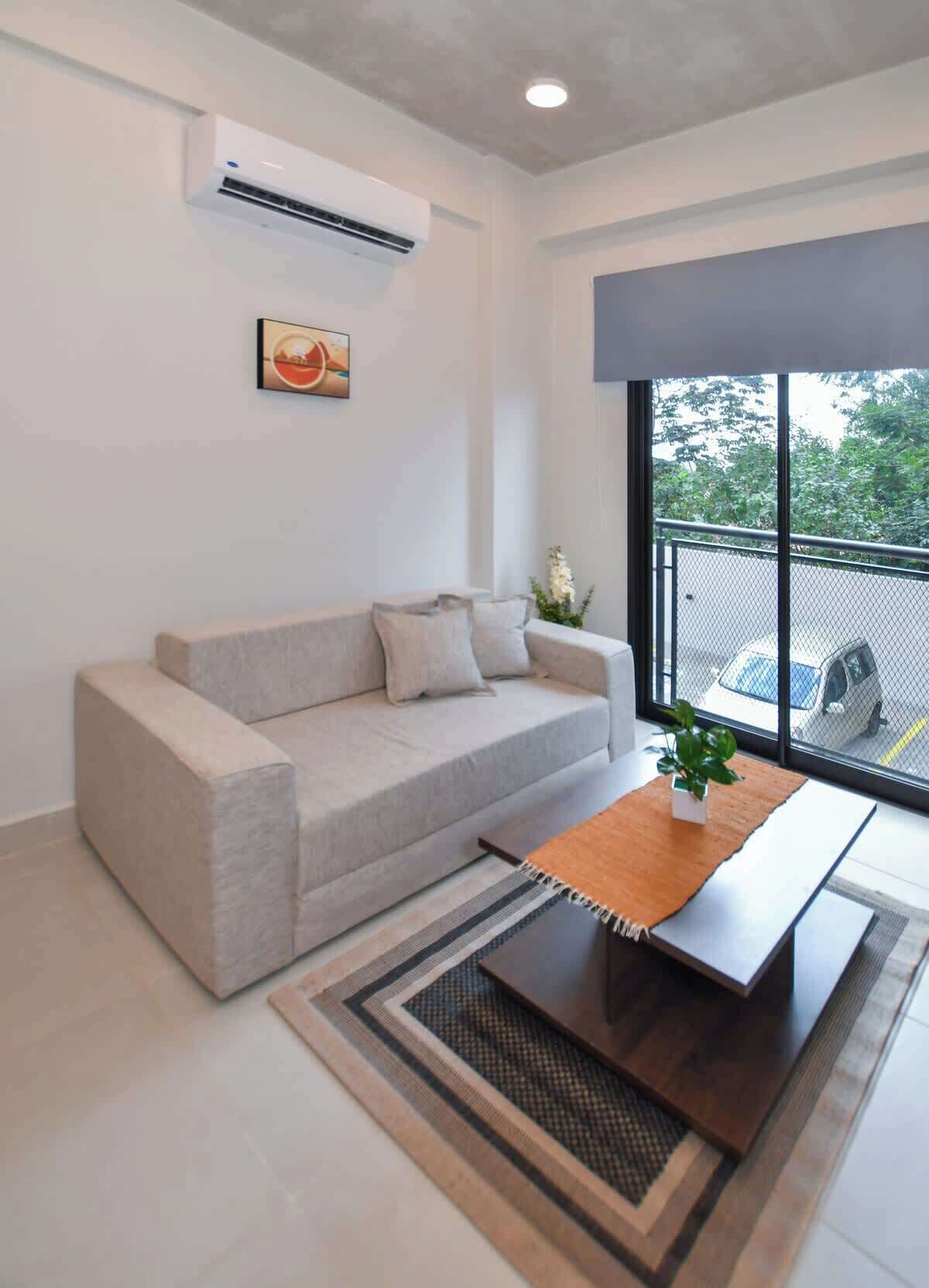 A modern living room with a sofa, a coffee table, and a large window with a view of the street.
