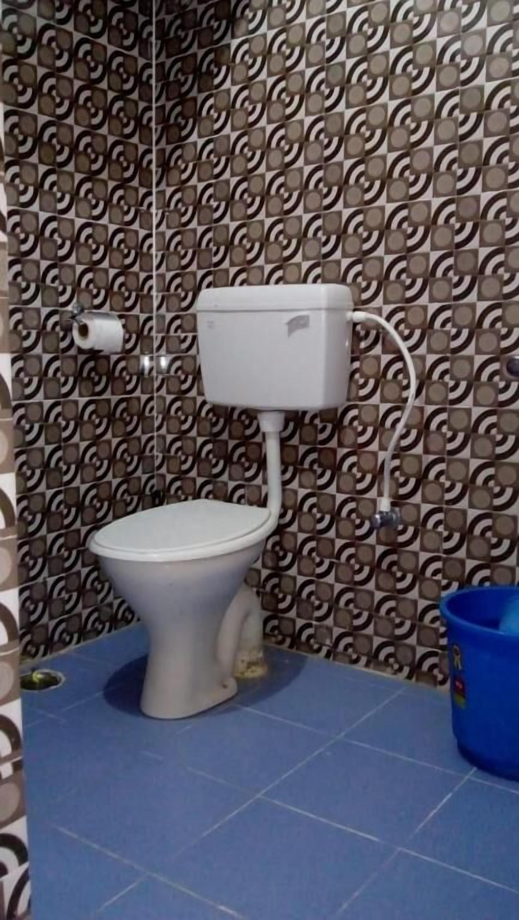 Une salle de bain avec des toilettes, un seau bleu et des murs à motifs.