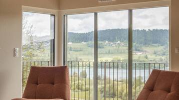Ein geräumiges Zimmer mit zwei braunen Sesseln, einem Holztisch und großen Fenstern mit Blick auf eine Landschaft.