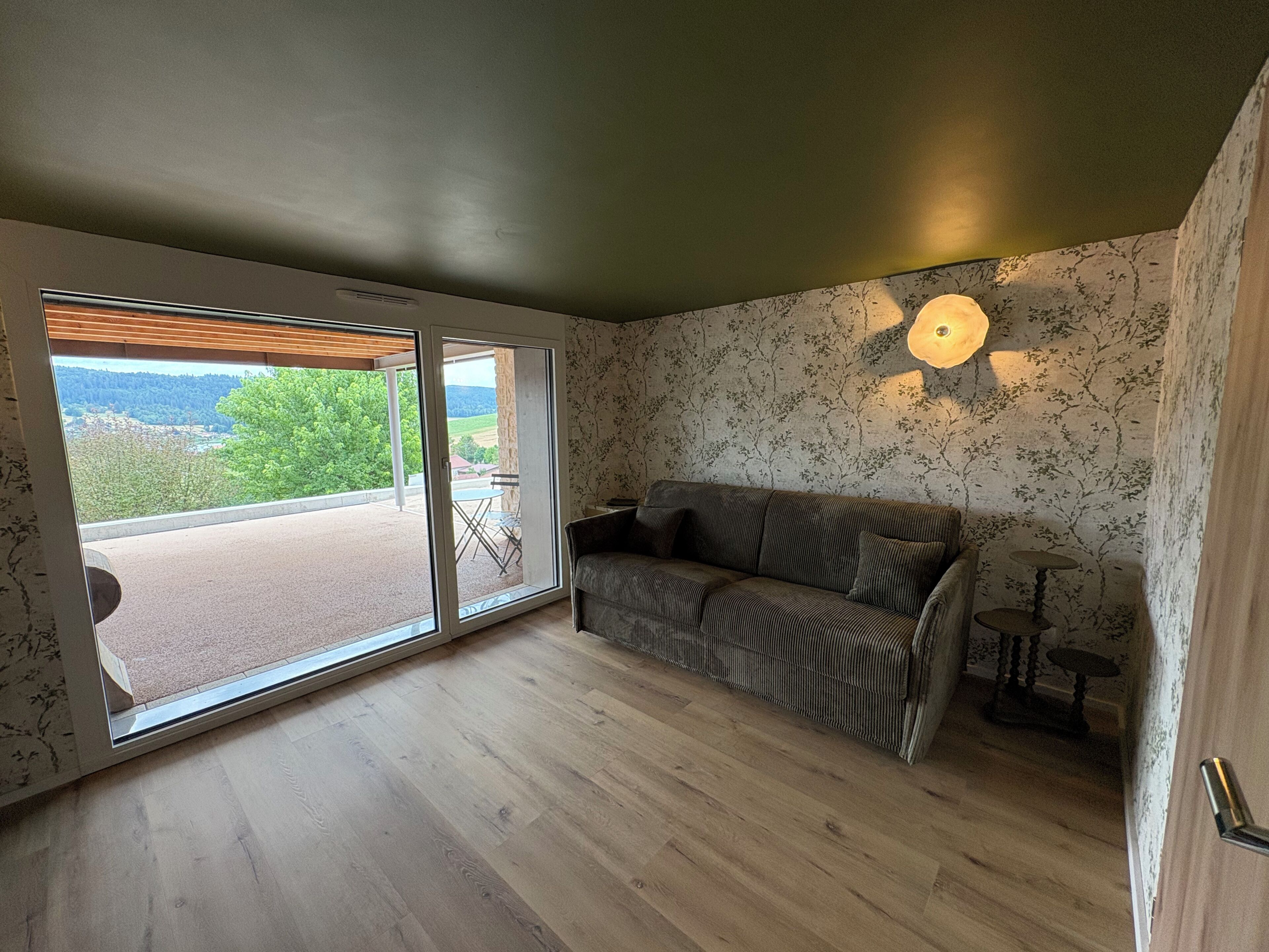 Habitación con puerta corrediza de vidrio que da a un área exterior, un sofá, una mesita y una lámpara fijada a la pared.