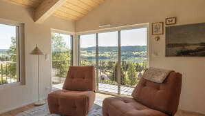 Il s'agit d'une pièce spacieuse avec un plafond haut, de grandes fenêtres et une vue sur un paysage. On y trouve deux fauteuils et une table.
