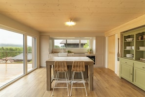 A modern kitchen with a wooden table and chairs, a view of the outdoors, and a green cabinet with dishes. - Between the Lake and the Jura, Luxury Home—Sleeps 6—View of Lake St. Point: Luxury and Cozy Comfort (Les Grangettes)