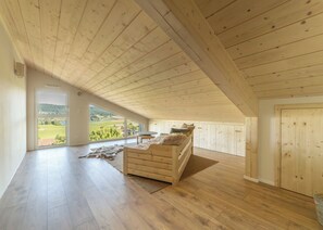 Ein geräumiges Schlafzimmer im Dachgeschoss mit Holzbalkendecke, einem großen Fenster mit Blick auf die Landschaft, einem Bett mit Felldecke und einem kleinen Tisch.