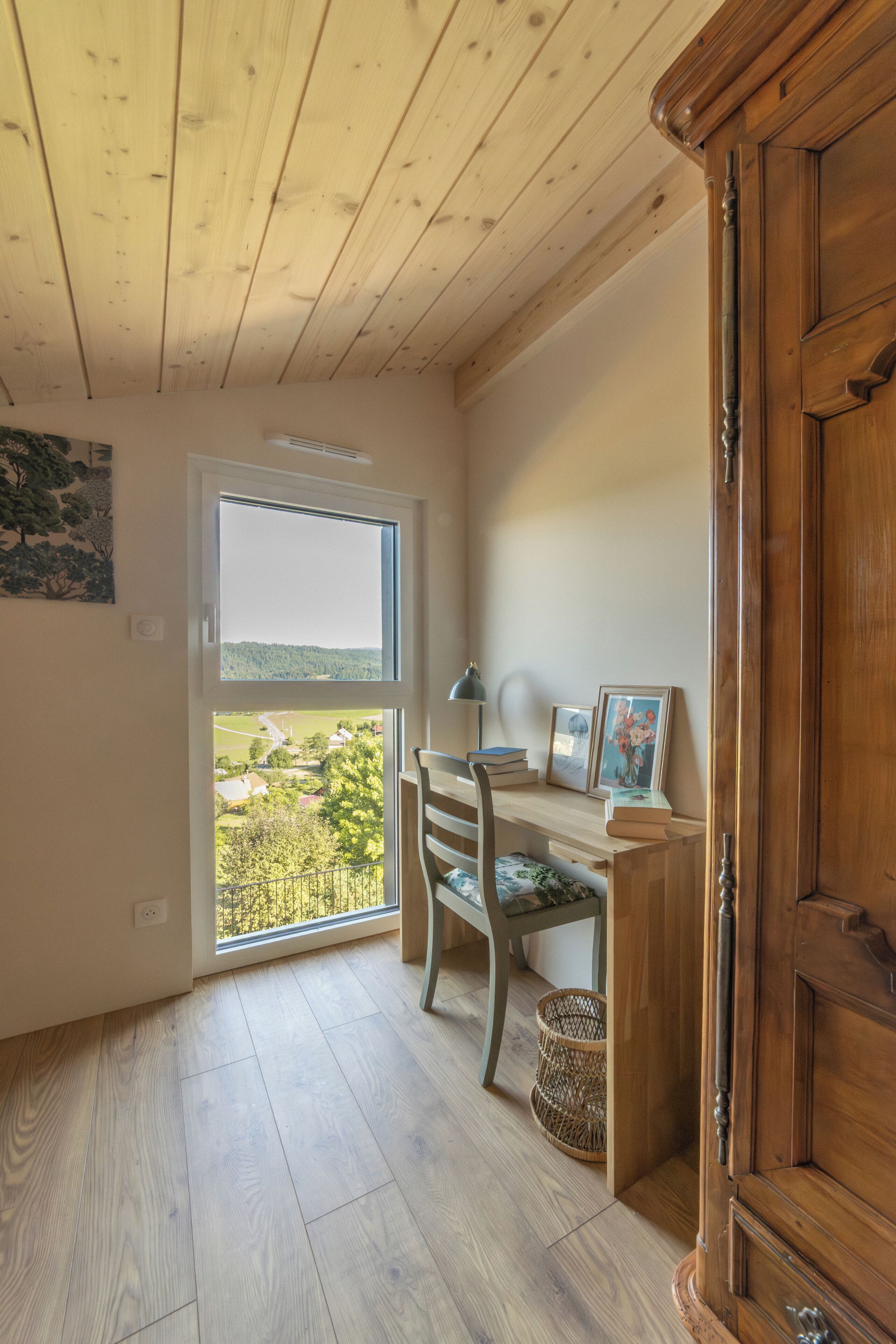 Une pièce comprenant un bureau en bois, une chaise, une fenêtre donnant sur un paysage et un meuble en bois.