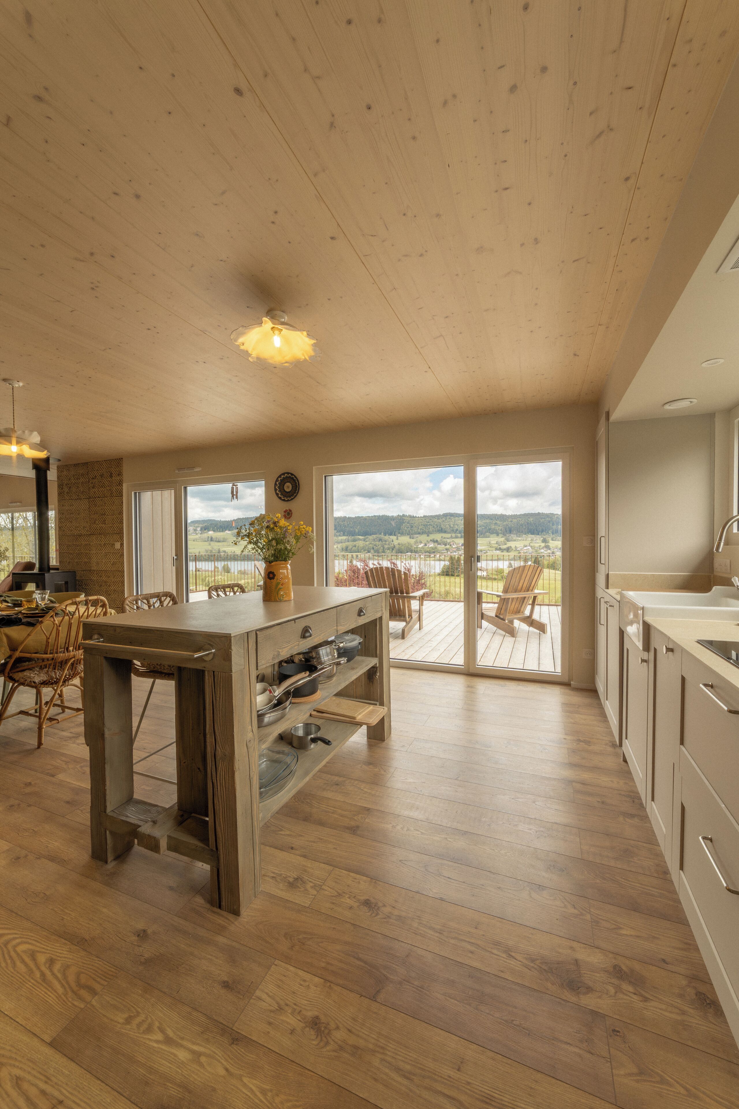 Un'ampia cucina con pavimento in legno, un'isola centrale e vista all'esterno tramite ampie finestre.