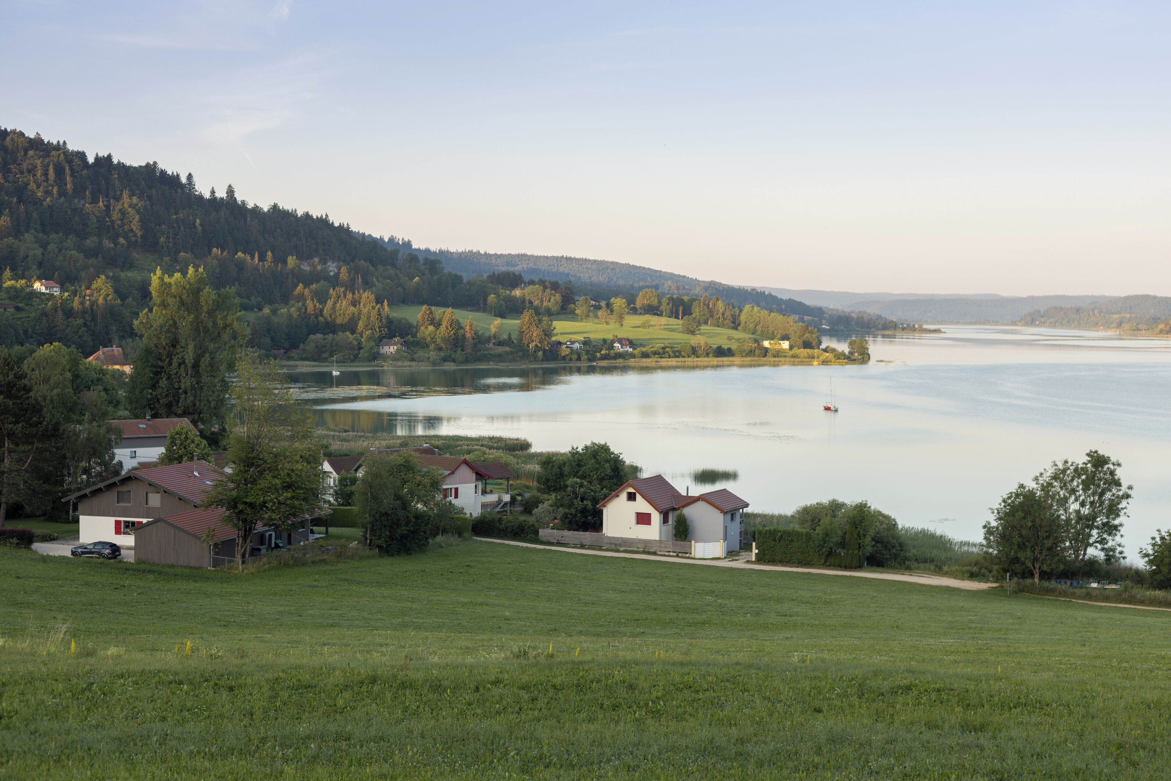Une propriété au bord du lac comprenant plusieurs maisons, un terrain verdoyant au premier plan et une colline boisée en arrière-plan.