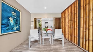 A hotel corridor with a large painting, a dining area with chairs and a table, and a bamboo wall.