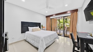 A hotel room with a bed, a desk, a TV, and a sliding glass door to a balcony.