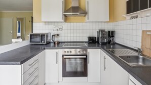 Moderni keittiö, jossa on valkoiset kaapit, ruostumattomasta teräksestä valmistettu uuni, mikroaaltouuni, kahvinkeitin ja pesuallas.
