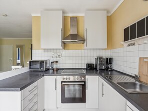 A modern kitchen with white cabinets, a stainless steel oven, a microwave, a coffee maker, and a sink. - Coastal Holiday Apartment near Kühlungsborn (Bastorf)
