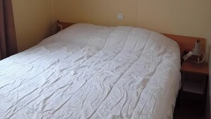 Een slaapkamer met een enkel bed, houten kasten erboven en een nachtkastje met een lamp.