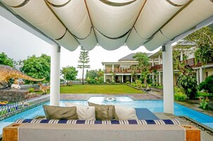 A poolside area with a covered seating area, a dinosaur statue, and a view of a building with a garden.