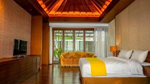 A hotel room with a bed, a TV, a sofa, and a view of greenery outside.