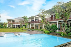 A hotel with a swimming pool, multiple balconies, and lush greenery.
