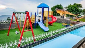 A playground with swings, slides, and a dinosaur statue.