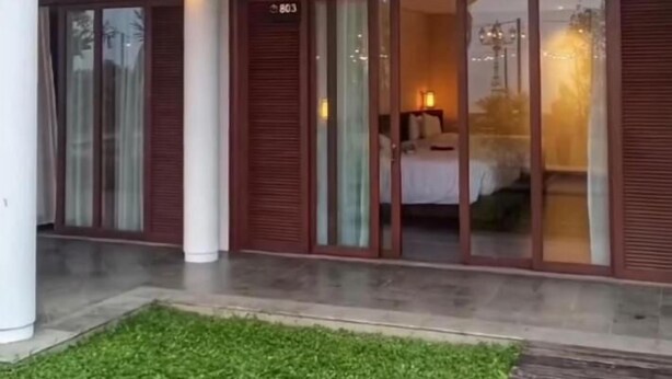 A modern hotel entrance with a covered patio, large sliding glass doors leading to a bedroom, and a well-maintained lawn.