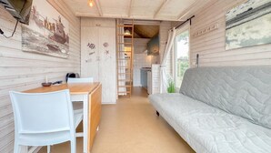 Interior de una cabaña con comedor, sofá, cocina y un amplio ventanal.