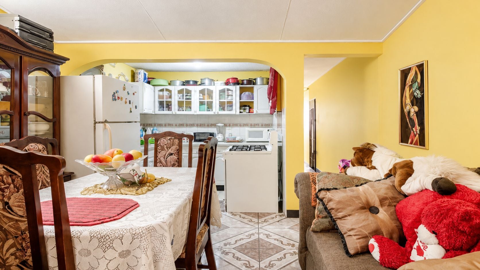 Un comedor con una mesa preparada para dos, una cocina al fondo y una sala de estar con un sofá y juguetes de peluche.