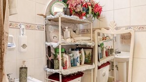 Kylpyhuone, jossa on wc, pesuallas ja hyllyjä, joilla on hygieniatuotteita.