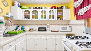 Une cuisine avec des meubles blancs, une cuisinière à gaz, un four à micro-ondes et divers ustensiles de cuisine.