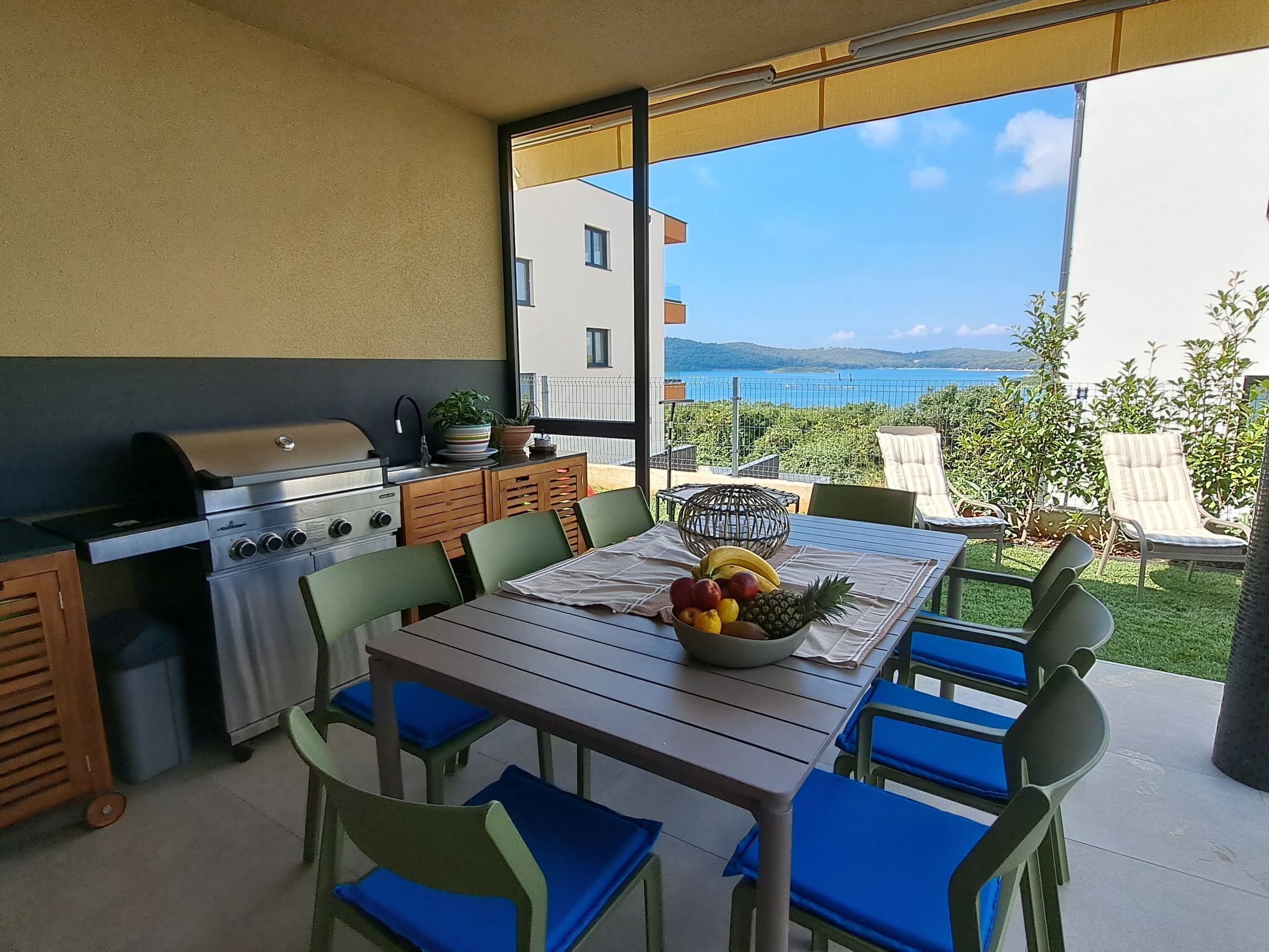 An outdoor kitchen with a grill, dining table, chairs, and a view of the sea.