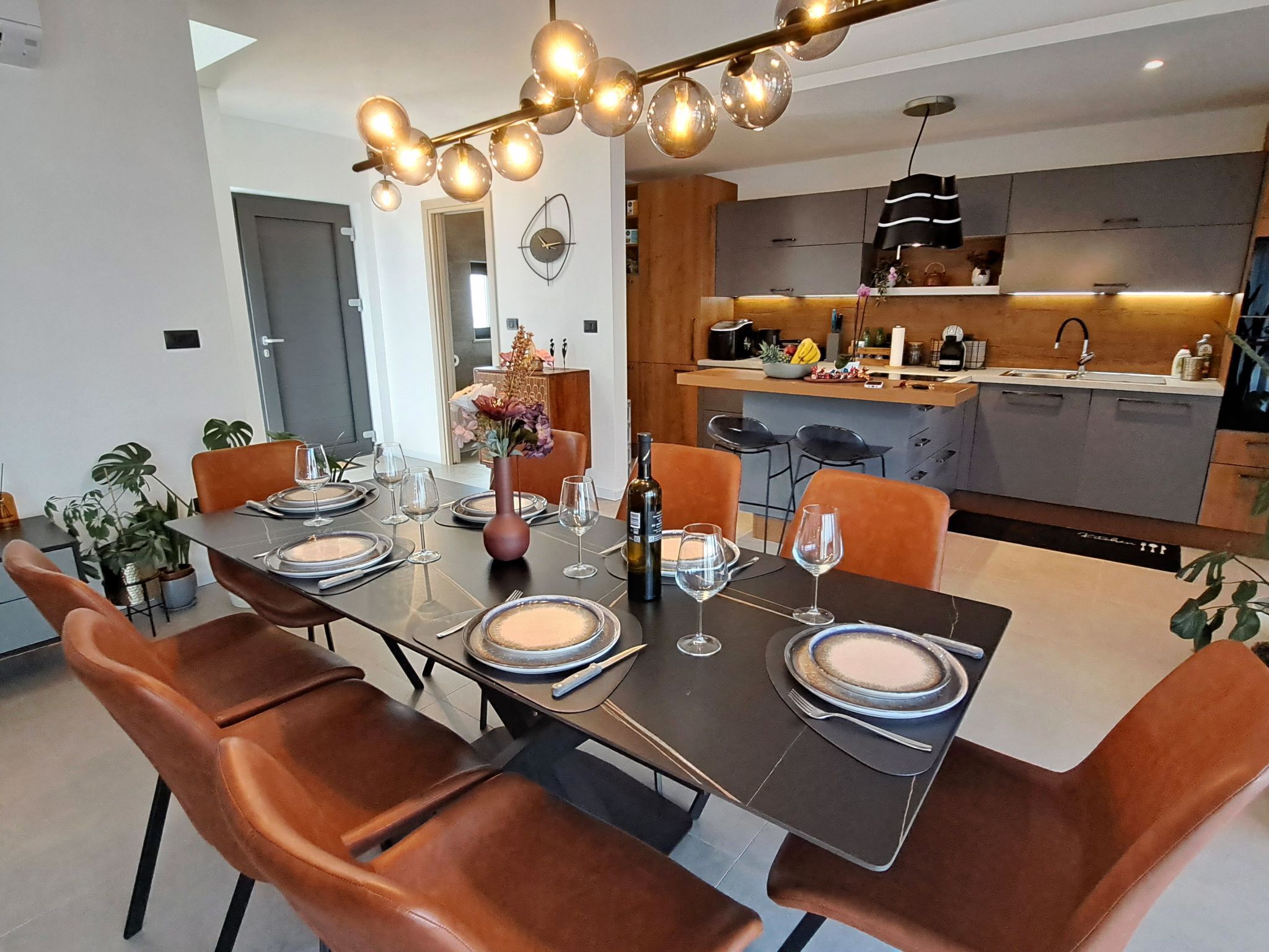A modern dining area with a long table set for six, surrounded by brown chairs.