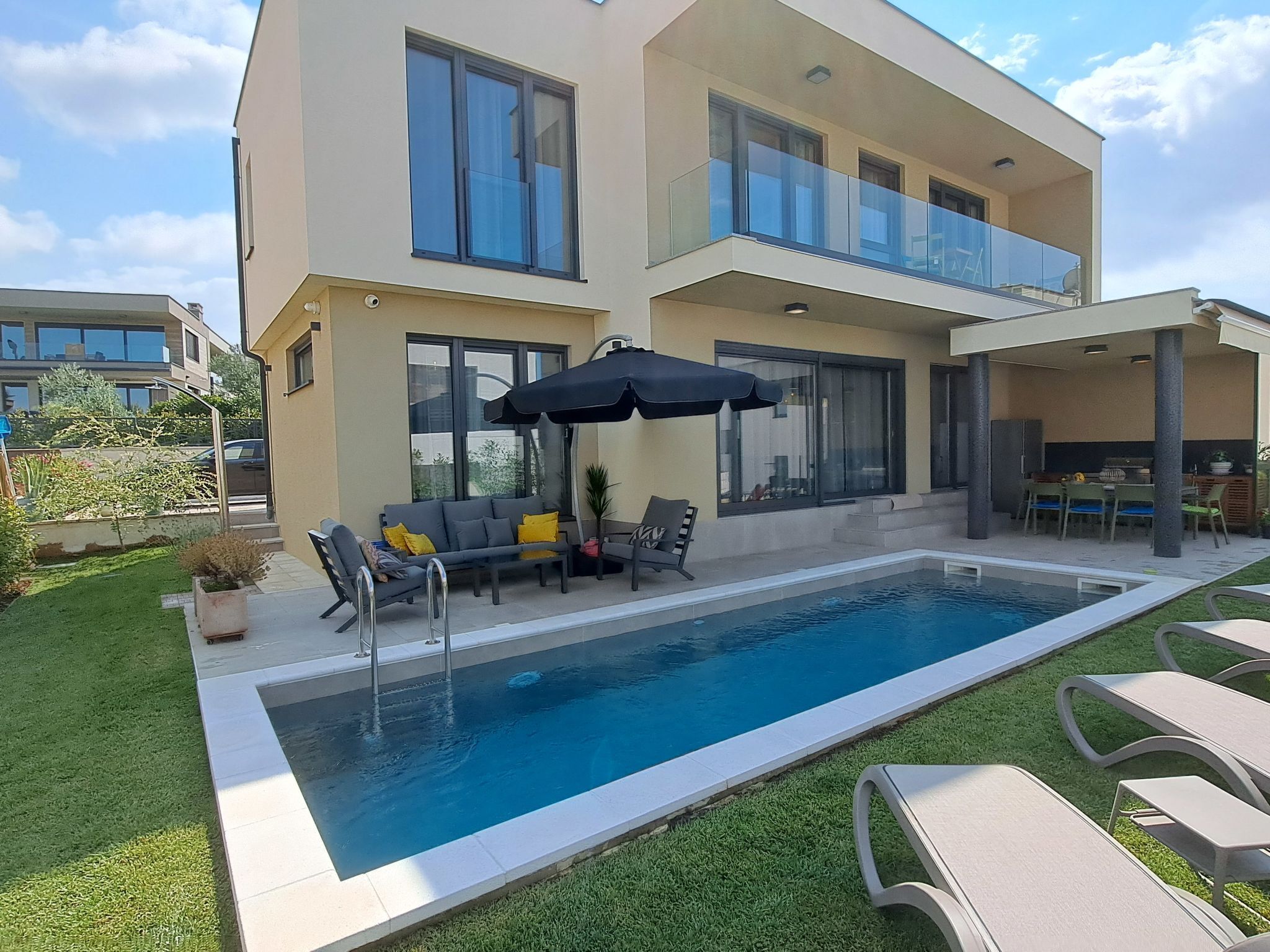 A modern two-story house with a swimming pool, outdoor furniture, and a covered patio area.