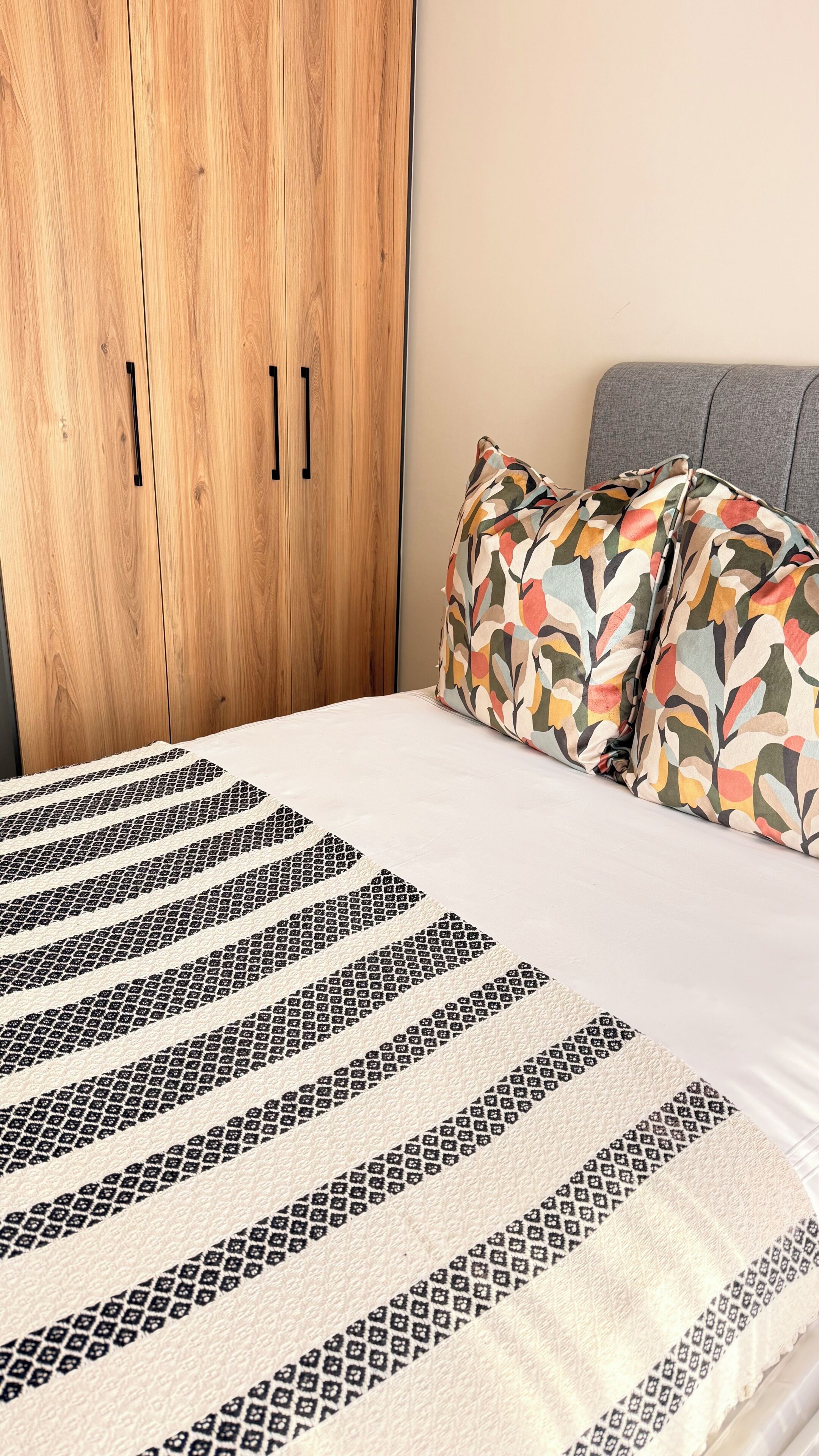 Un dormitorio con un armario de madera, un edredón estampado y almohadas coloridas.