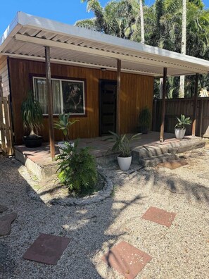 A wooden house with a covered porch, potted plants, and a gravel driveway.
