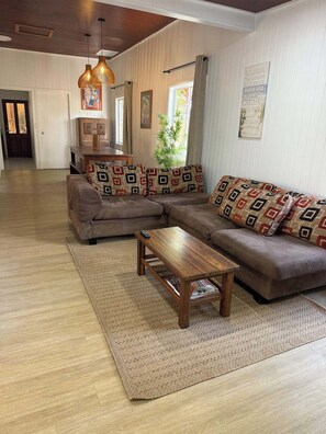 A living room with a sectional sofa, a wooden coffee table, and a patterned rug. - Barefoot@Belongil (Byron Bay)