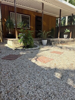 A covered outdoor area with a gravel ground, wooden steps leading to a door, and potted plants.