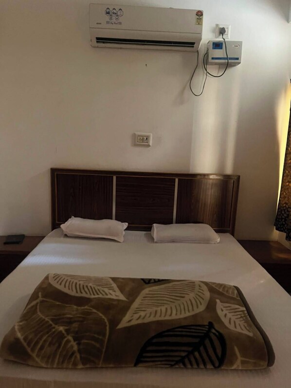 A hotel room with a bed, a wall-mounted air conditioner, and a power outlet.