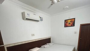 Un dormitorio con cama, aire acondicionado, ventilador de techo, una puerta y un cuadro colgado en la pared.