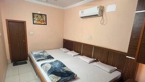 Un dormitorio con cama, ventilador de techo, aire acondicionado, puerta de madera y un cubo de basura azul.