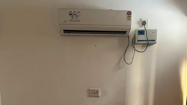 Habitación de hotel con cama, cabecera, unidad de aire acondicionado, toma de corriente e interruptor de pared.