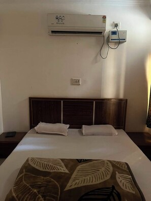 A hotel room with a bed, a headboard, an air conditioning unit, a power outlet, and a wall socket.