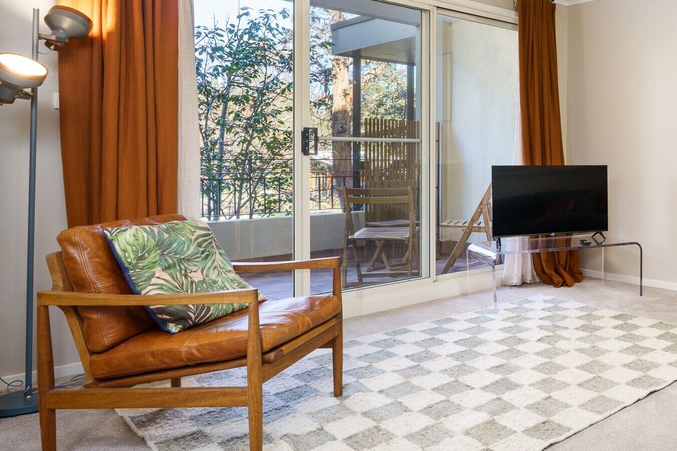 A room with a leather chair, a television on a stand, and a view through a glass door to an outdoor area.