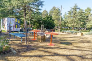 An outdoor area with seating arrangements, including benches and tables, surrounded by trees and a gravel path. - Haig Park and Braddon Dining at Your Doorstep (Braddon)