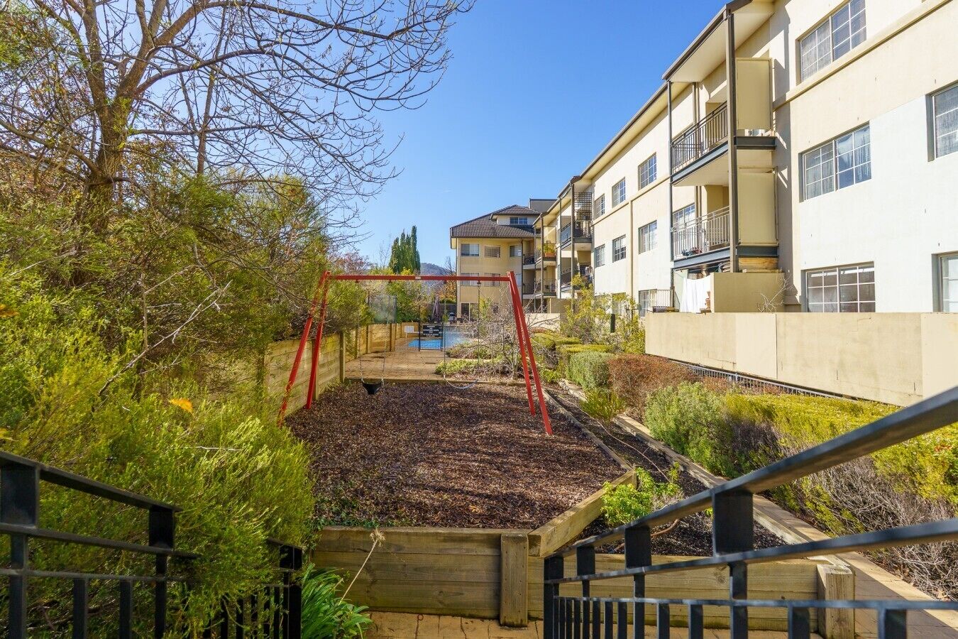 A residential area with a swing set, a swimming pool, and a building with balconies.