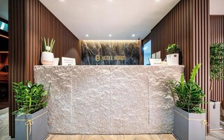 Un mostrador de recepción con encimera de mármol, paneles de madera a los lados y plantas en macetas.
