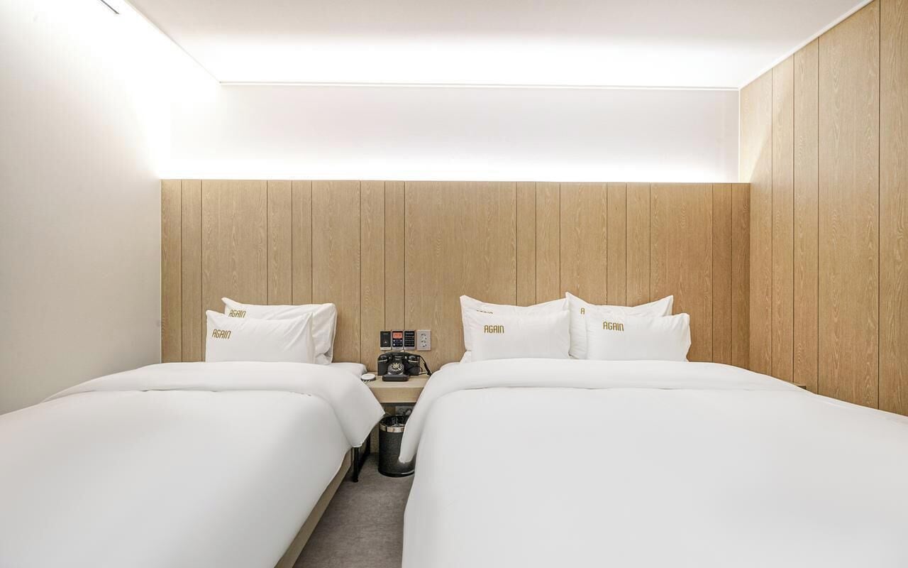A hotel room with two beds, wooden panel walls, a nightstand with a camera, and a trash bin.