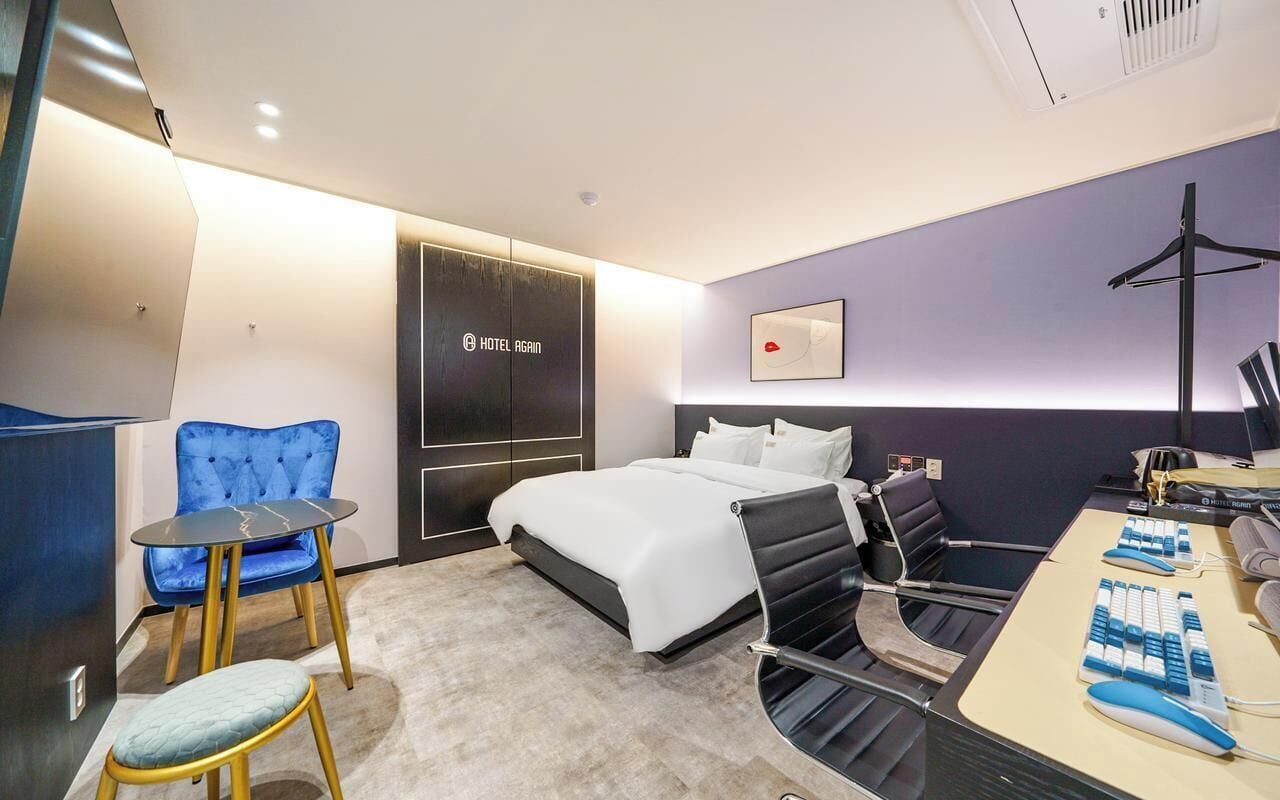 Habitación de hotel moderna con cama, escritorio, computadora, silla y una mesita.