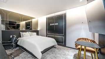 A modern hotel room with a large bed, a desk, a chair, and a wardrobe.