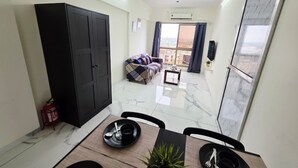 Et spiseområde med et bord dækket til to personer, en sofa i baggrunden og en sort garderobe.