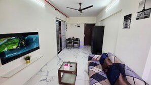 En moderne stue med et fladskærms-tv, en loftventilator, en sofa, et sofabord og et spiseområde.