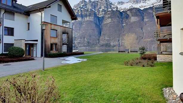 Un edificio moderno con tetto piatto e ampie finestre, sullo sfondo di montagne innevate.