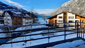 En moderne hytte med balkon med udsigt over et snækkedækket bjerglandskab og en sø.