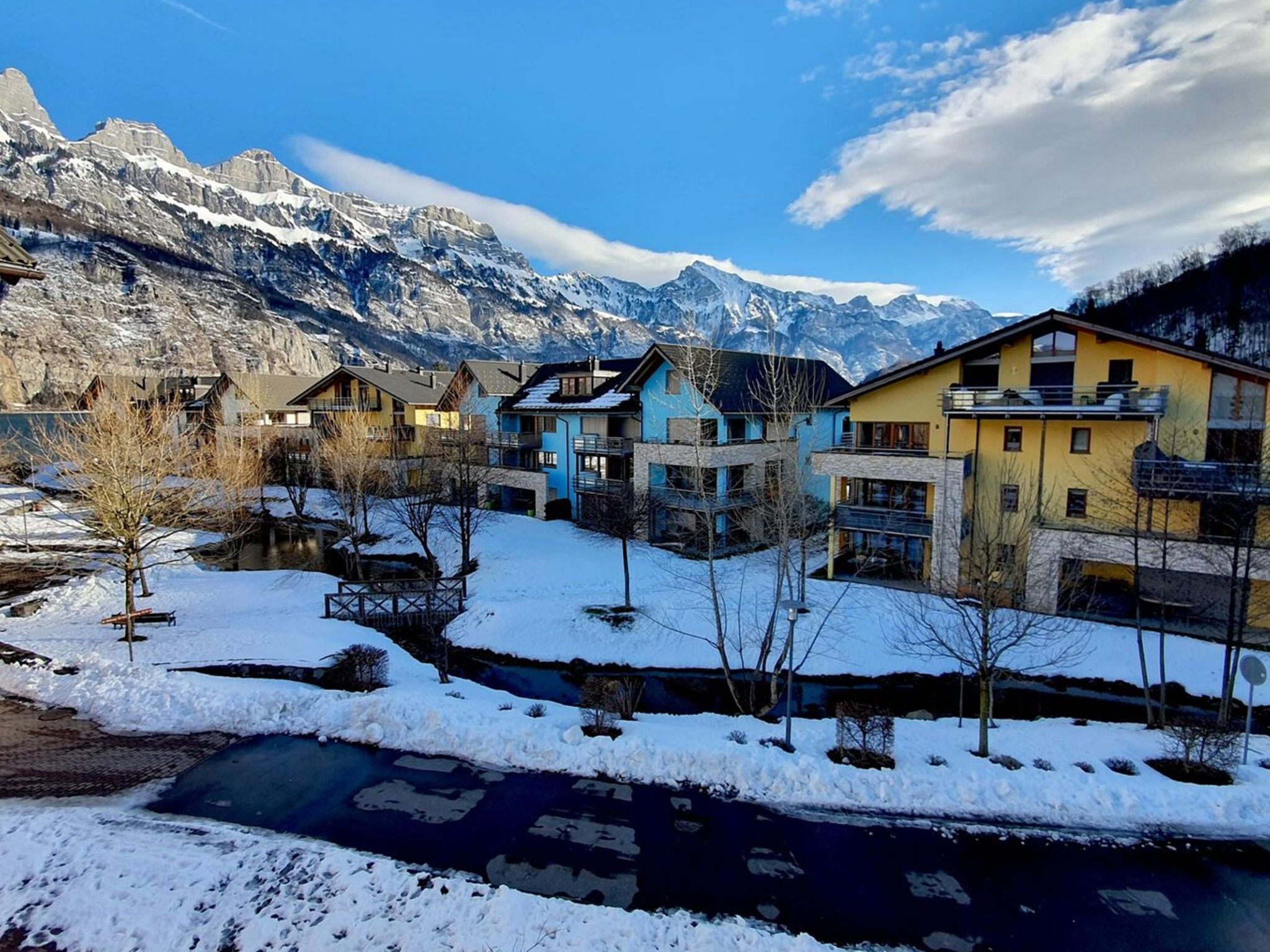 Un quartier résidentiel avec des maisons, une rivière et des montagnes en arrière-plan.