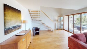 Et moderne interiør med en trappe i træ, et stort vindue og en rød sofa.