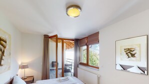 Et hotelværelse med seng, stol, bord, vindue og billeder på væggene.